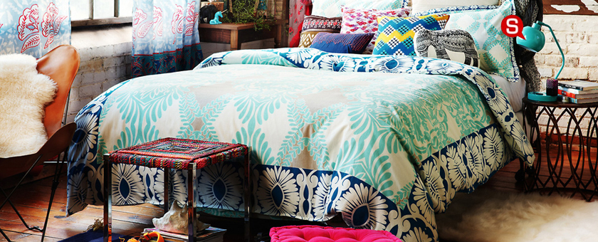 Au point central de la chambre à coucher dans le style boho se trouve un grand lit plein des coussins à motifs ethniques. L'arrangement est complété par de petites tables basses en différentes formes et couleurs.